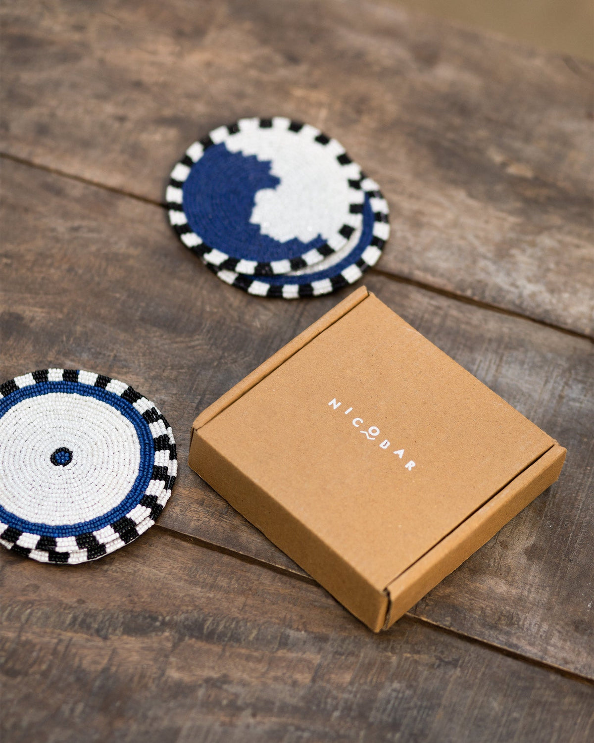 Dhaara Coasters beside a kraft gift box on a wooden table.