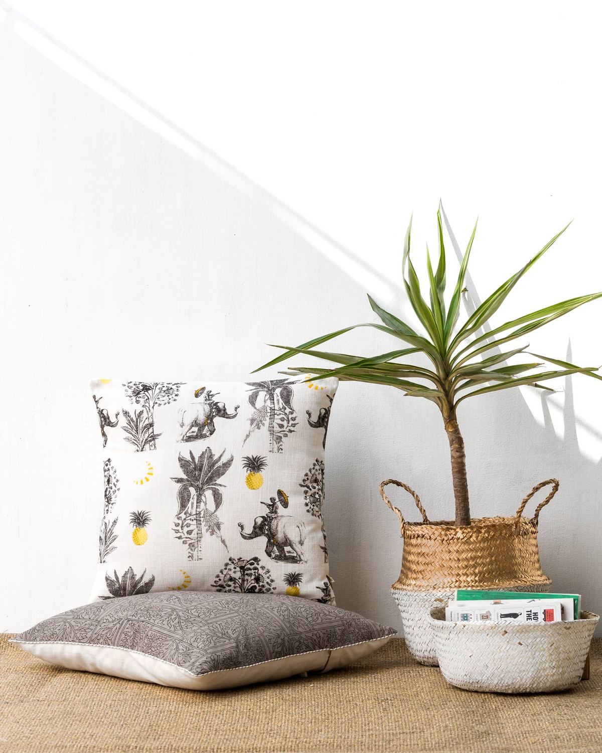Bentota Cushion Cover placed on the floor beside a potted plant.