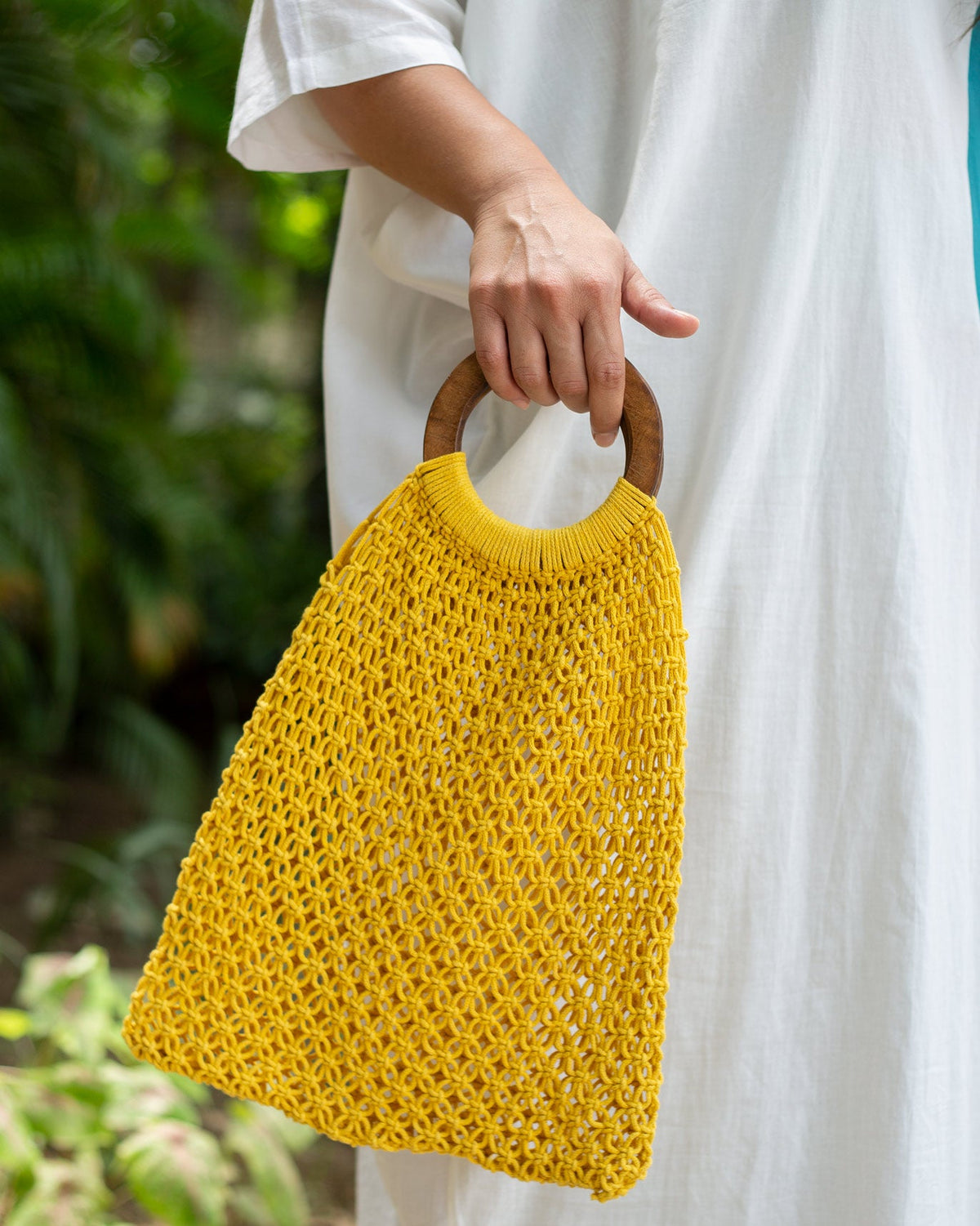 Person holding a yellow Mandovi Bag by its wooden ring handle.