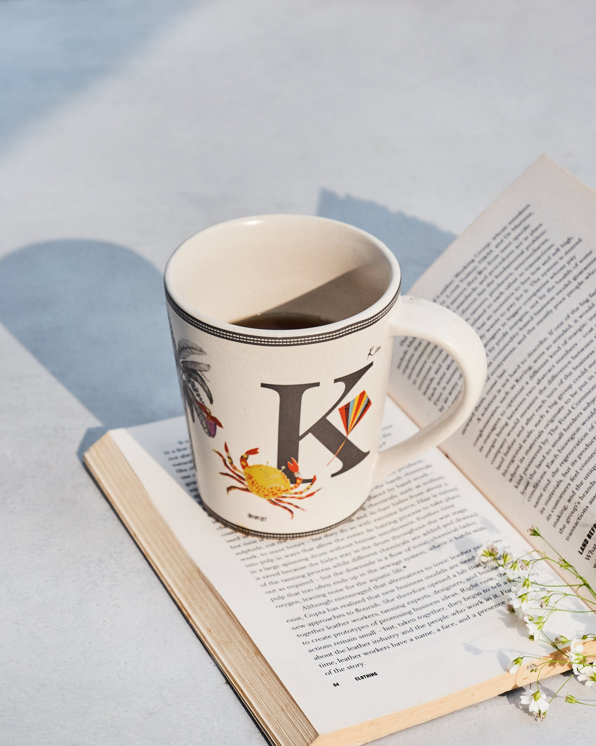 Cream Kamal mug with letter K motifs resting on an open book.