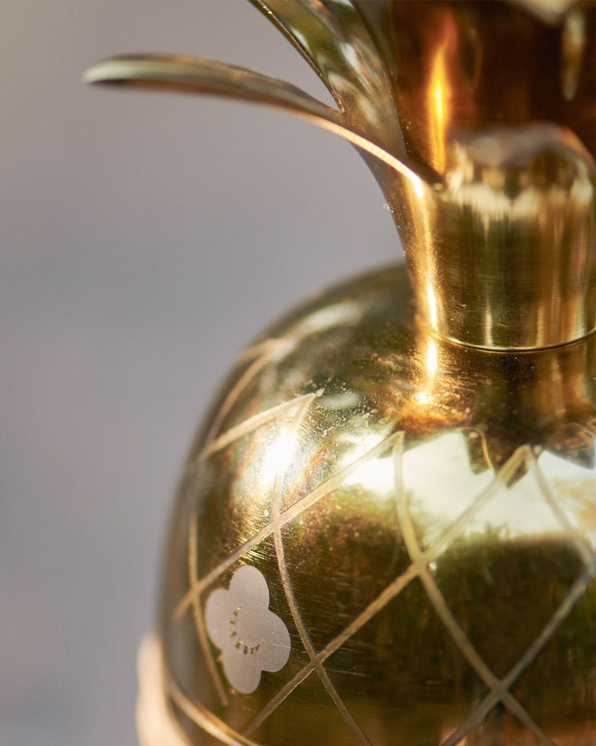 Close-up of the Ananasi cocktail shaker's gold pineapple body with a white flower motif.