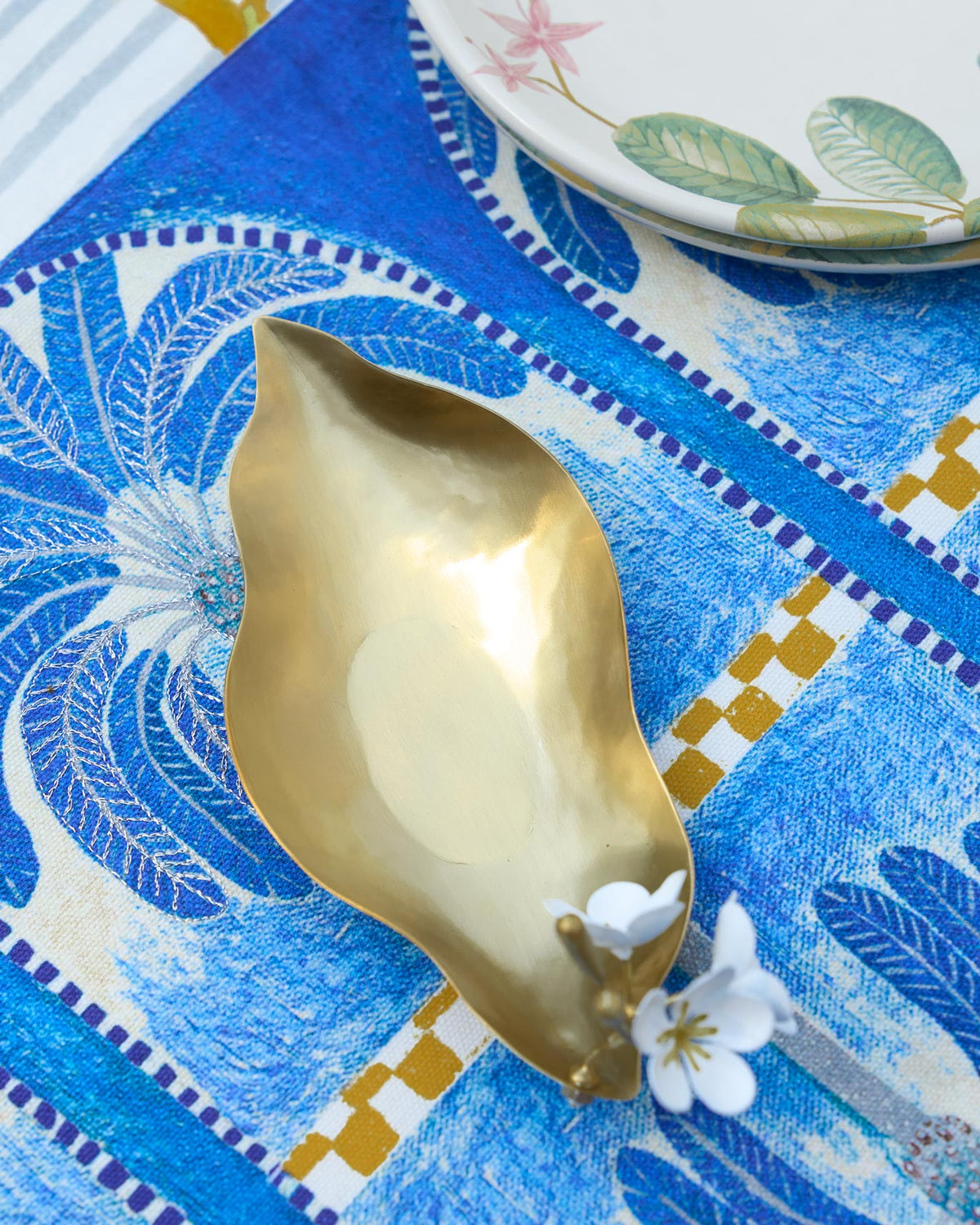 Champa Trinket Tray on a blue patterned cloth, with flowers at one end.