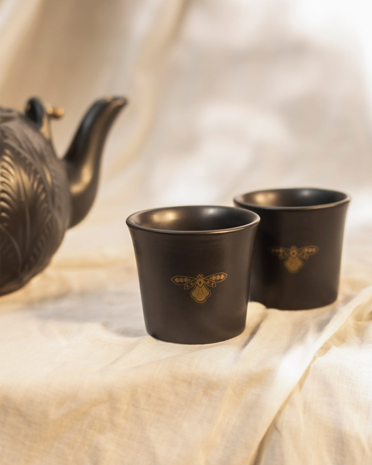 Moor teacups with gold moth motifs beside the embossed teapot.