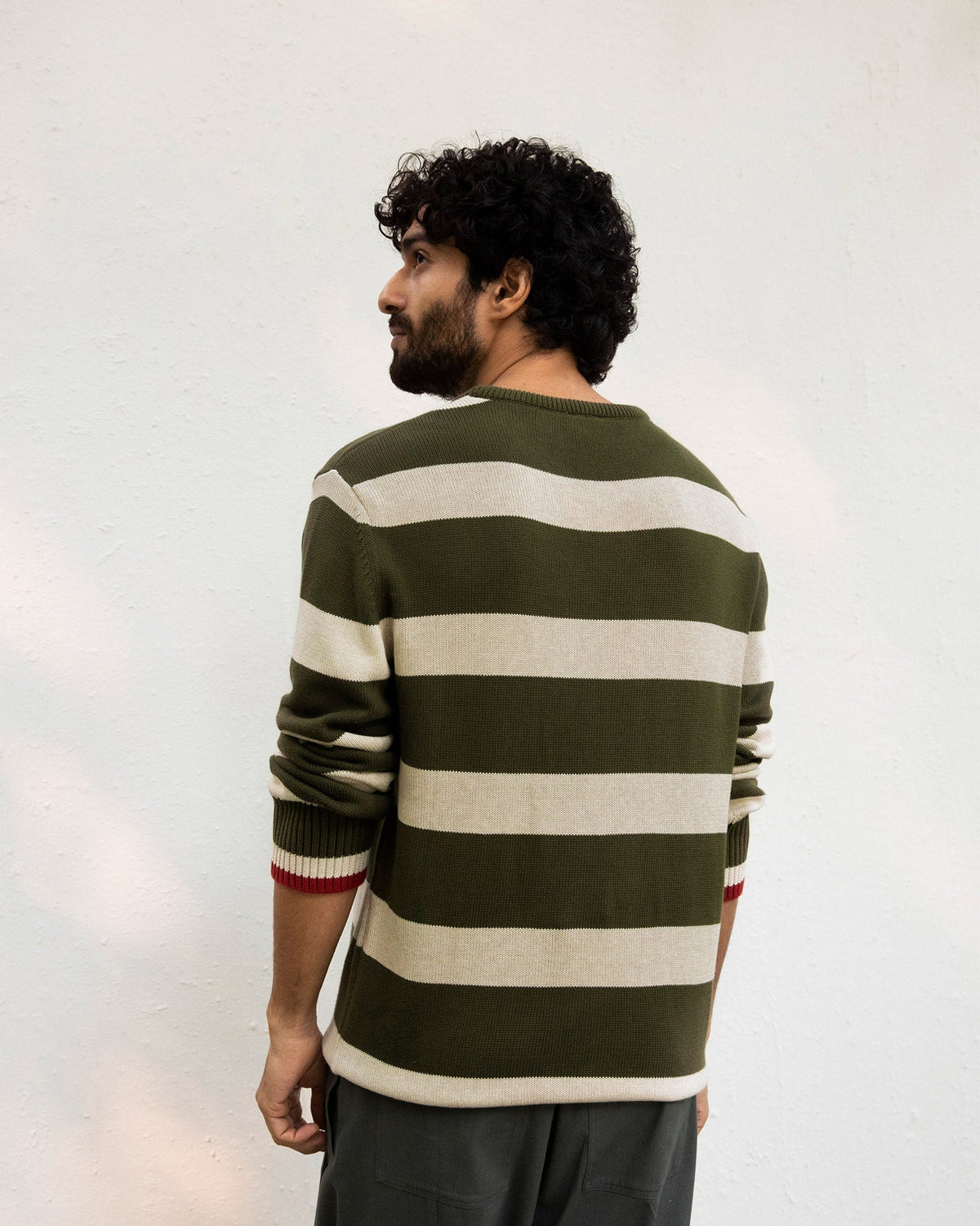 Back of an olive and oatmeal striped Round Neck Sweater with red cuff trim.