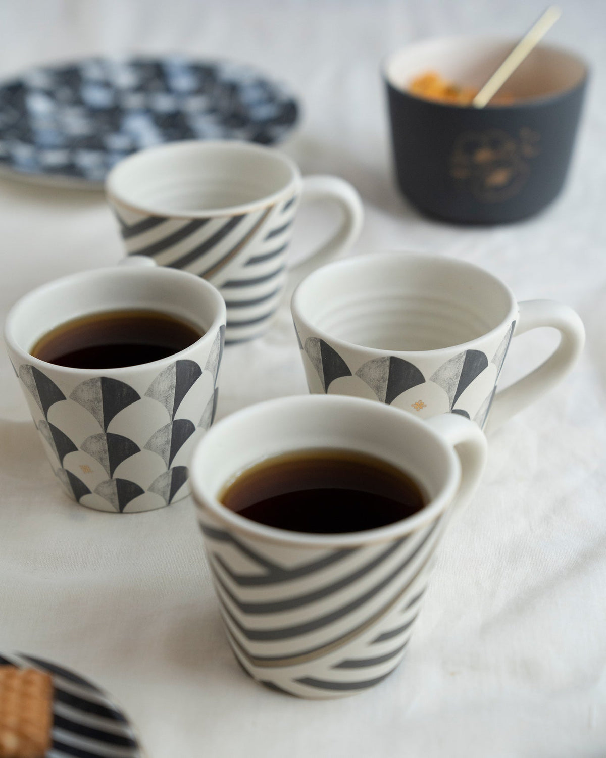 Khardung espresso mugs with charcoal patterns set on a white tablecloth.