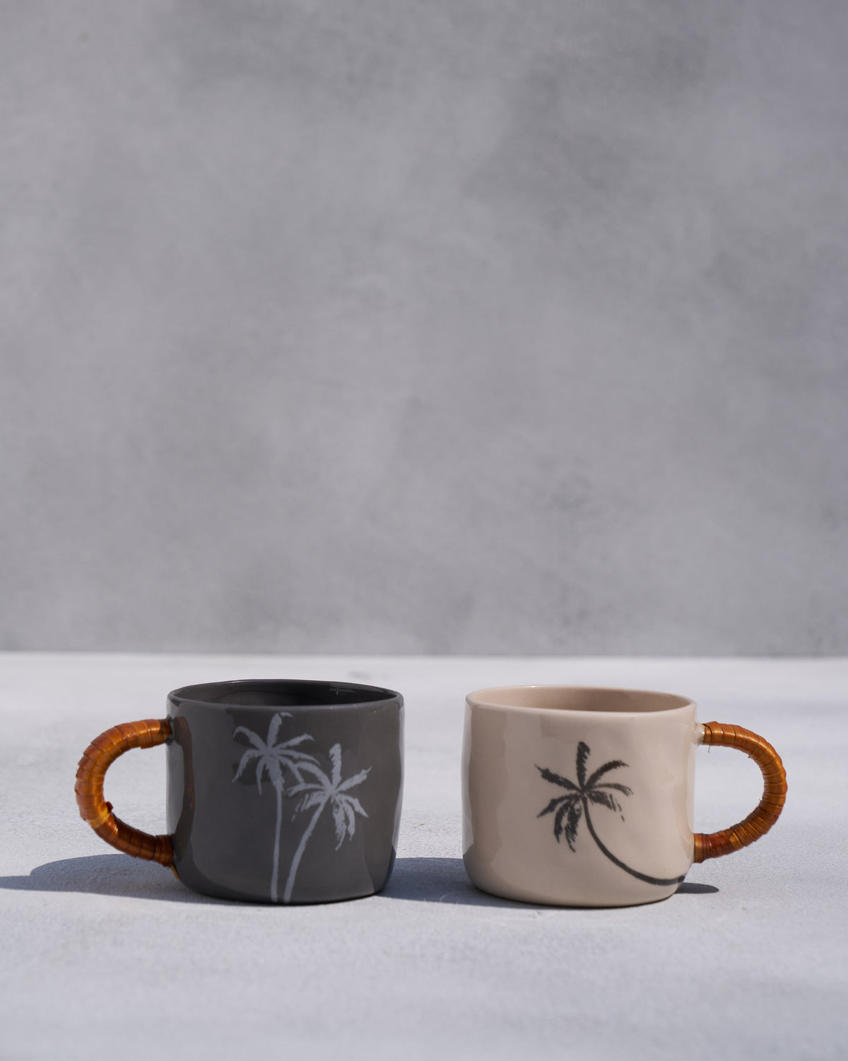 Charcoal and ivory Mandovi mugs with palm motifs and woven handles.
