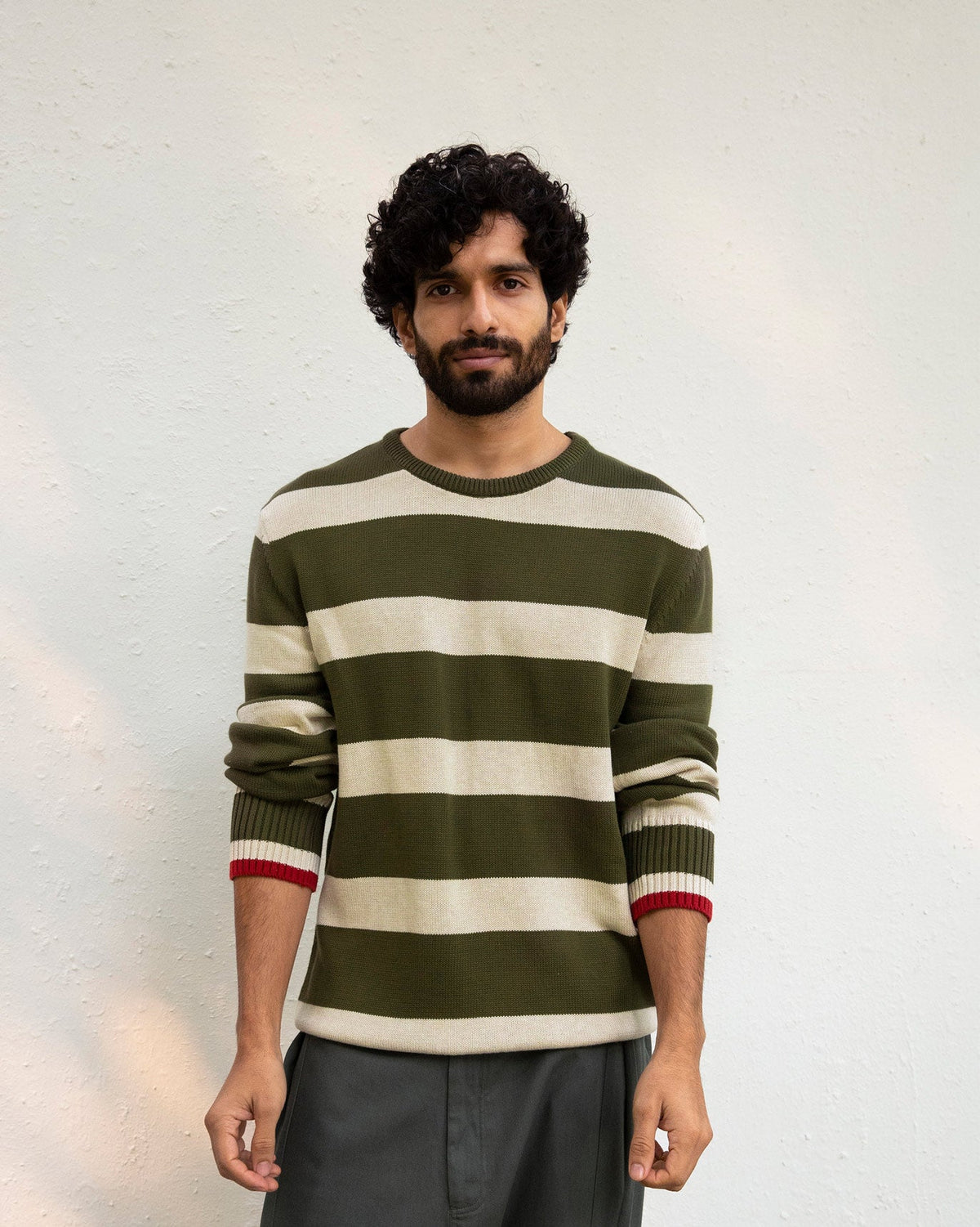 Person standing in a striped olive and oatmeal Round Neck Sweater with a crew neck.