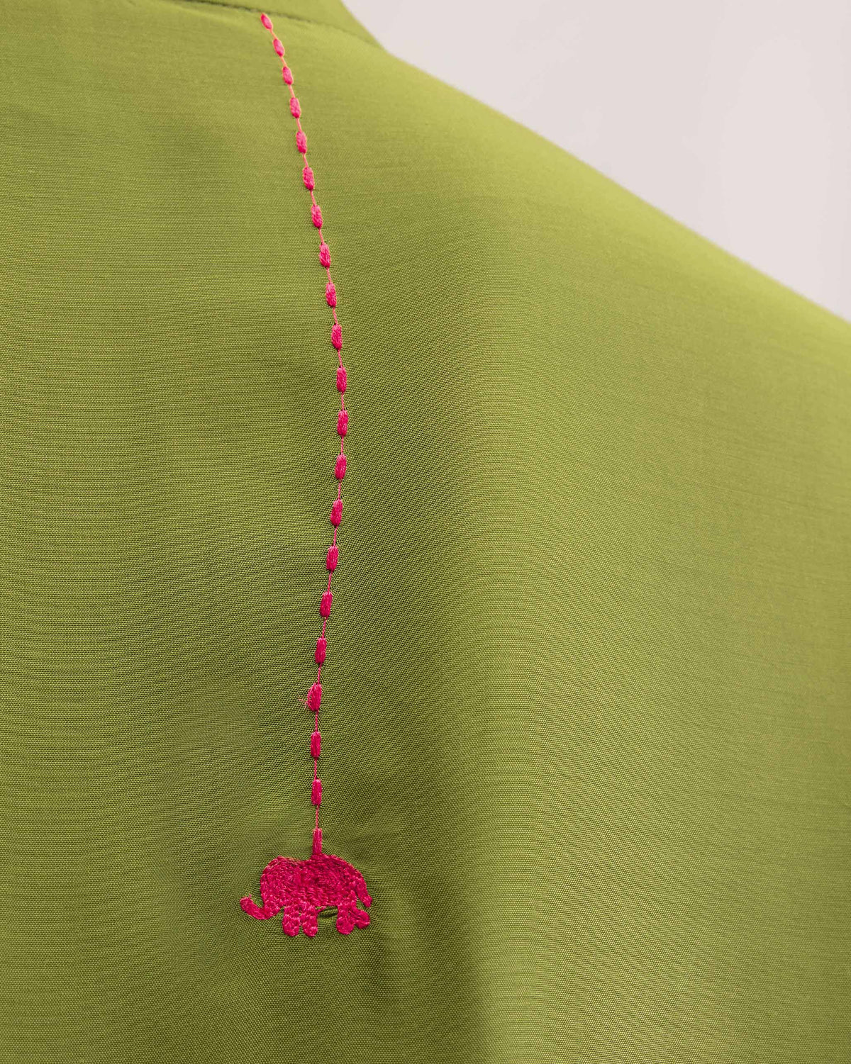 Close-up of a pink elephant embroidered on olive kurta fabric.