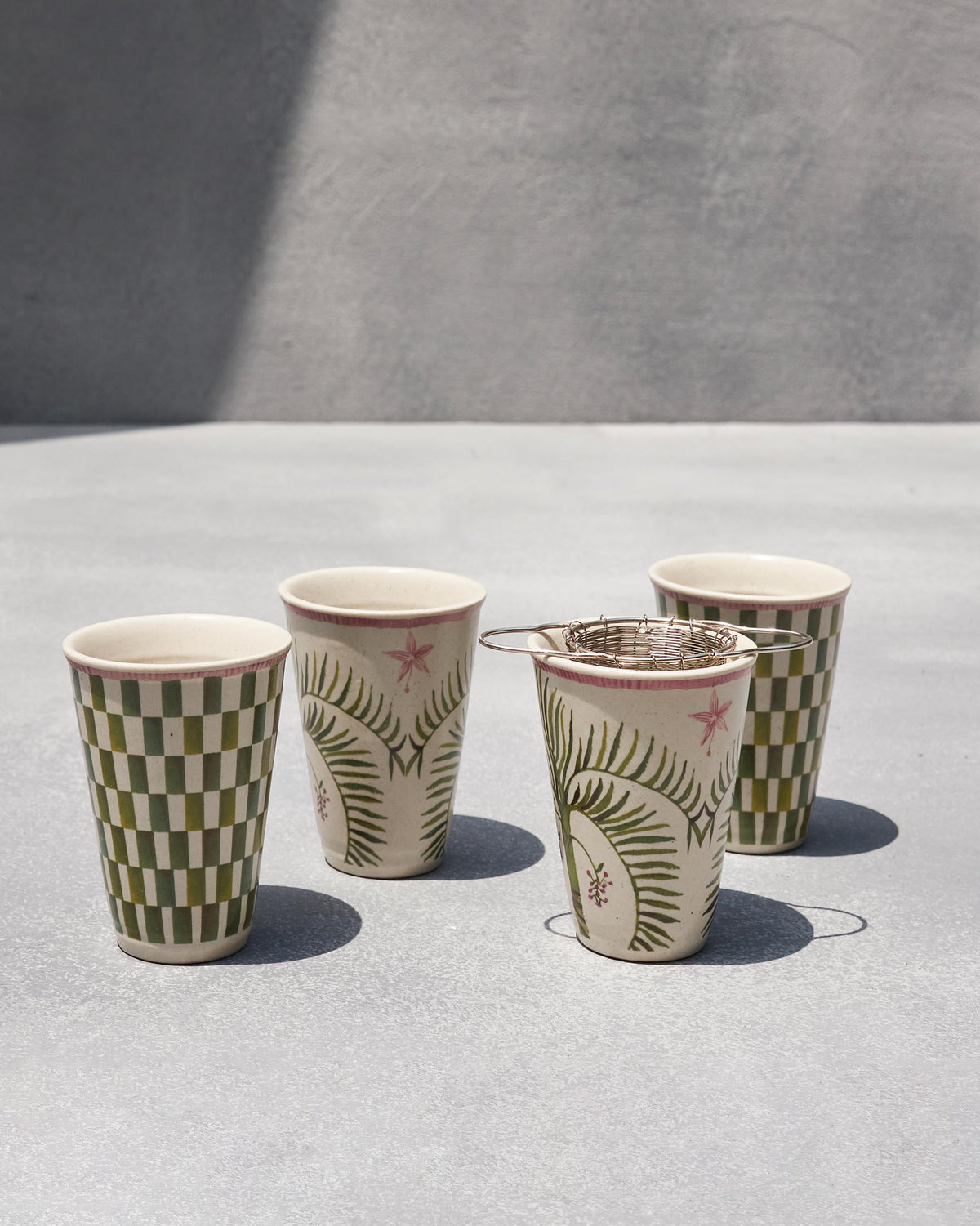 Four Oyster Bay kulhar cups in a row with a strainer resting on one.