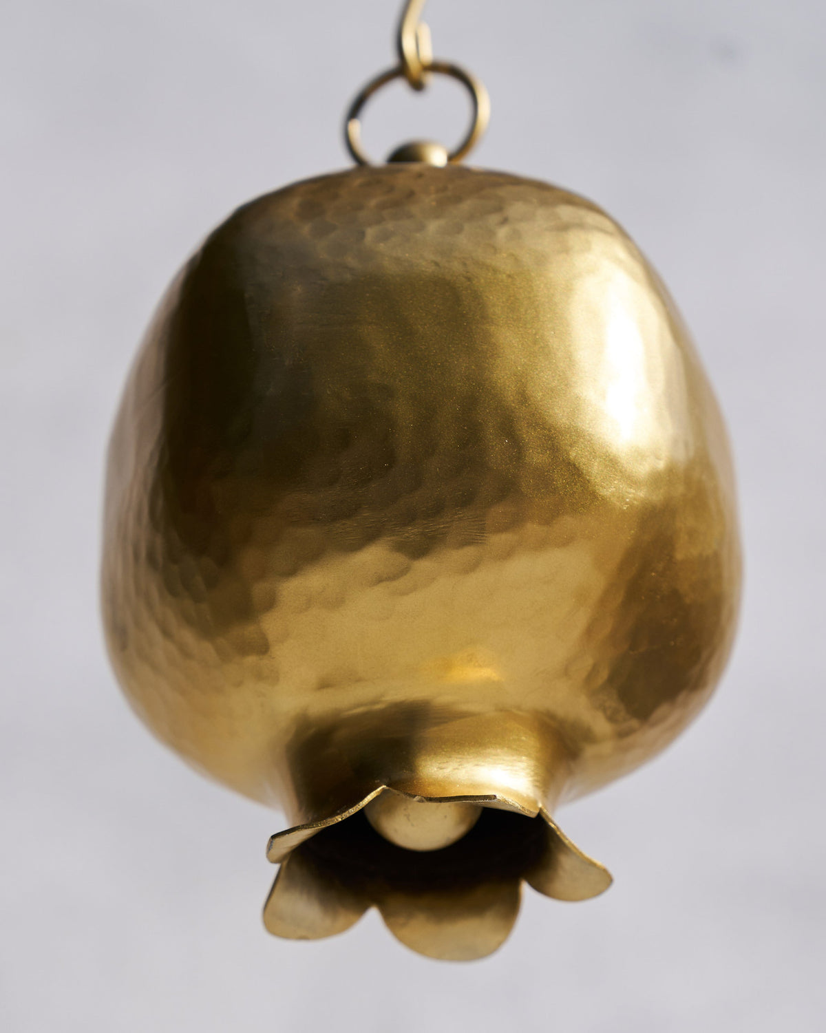 Close-up of a hammered gold Anar bell showing the clapper inside.