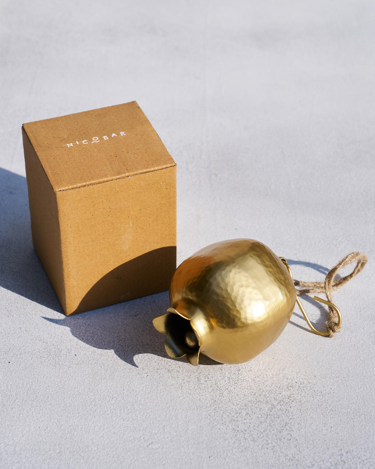 Hammered gold Anar bell beside a Nicobar gift box.