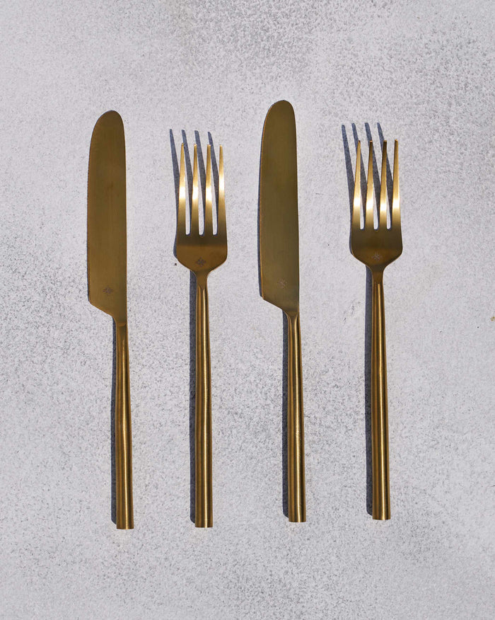 Set of four matte gold Sitara forks and knives laid in a row.