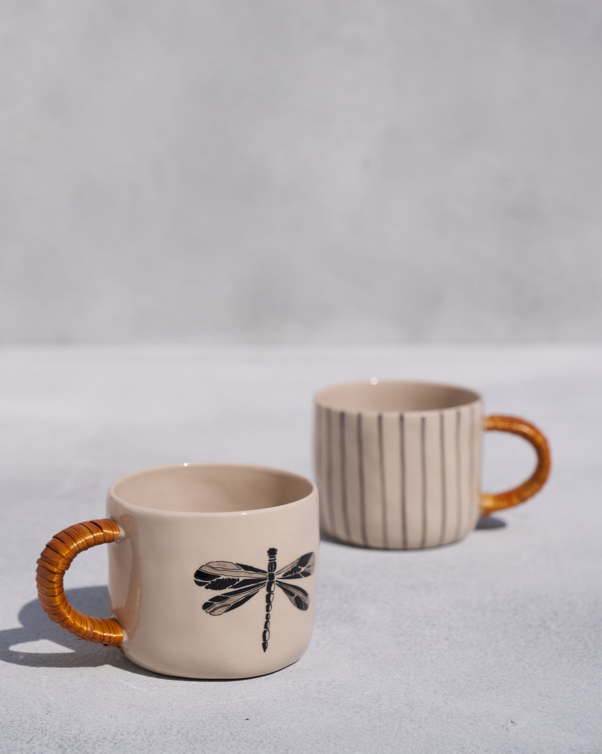 Cream mug with a black dragonfly print and cane handle beside a striped mug.