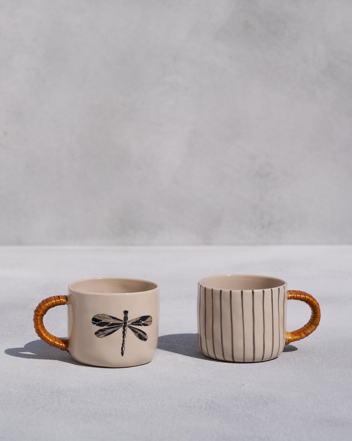 Set of two cream ceramic mugs with a dragonfly motif and vertical stripes.