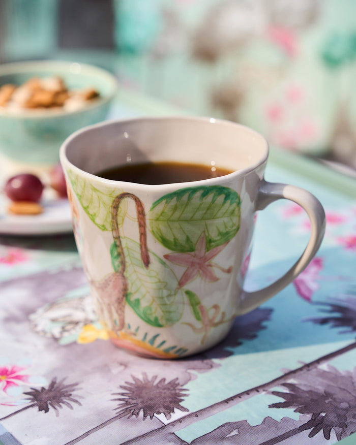 Cream mug with a macaque and cashew fruit motif filled with a dark drink.
