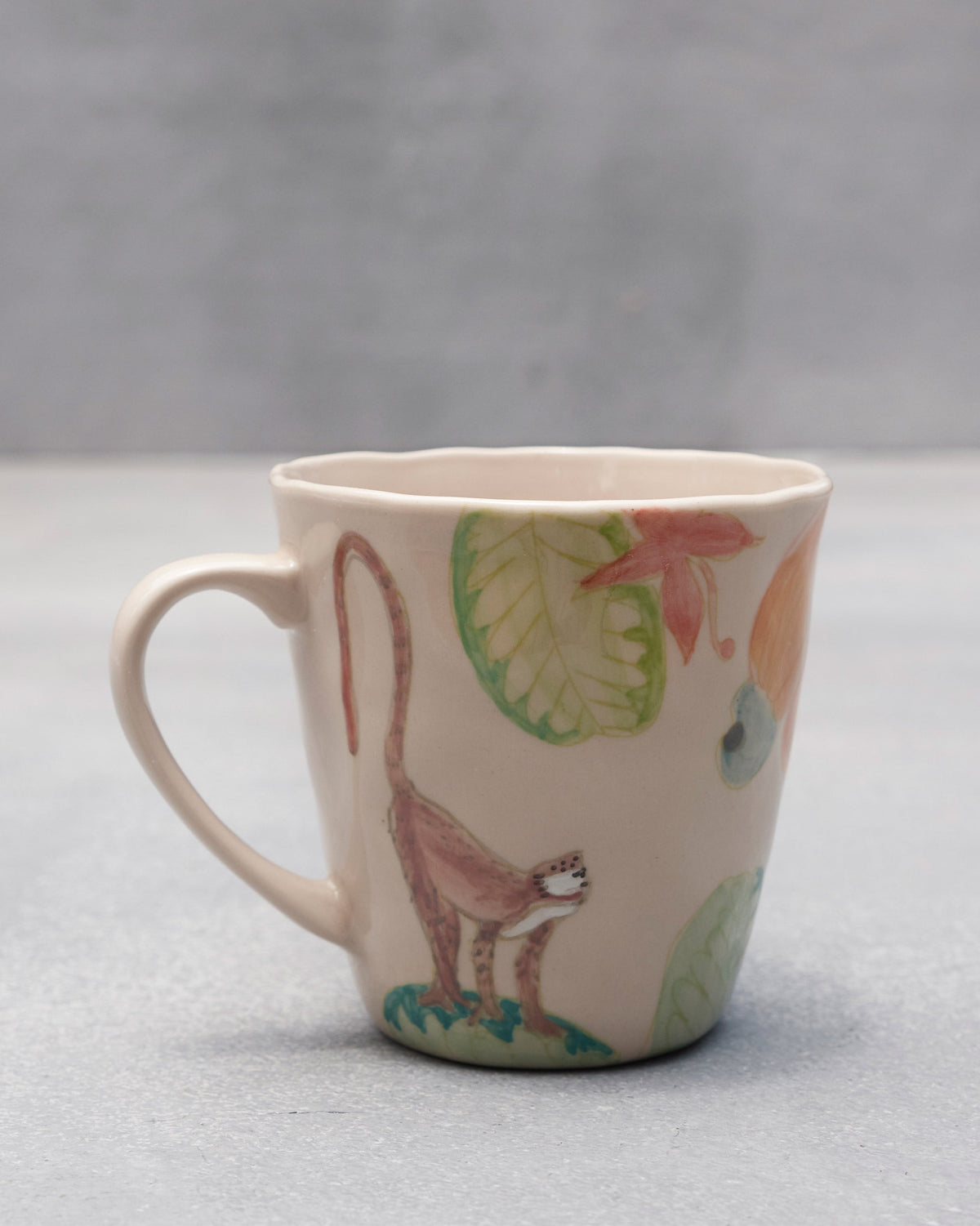 Cream ceramic mug with a macaque, cashew fruit, and tropical leaves.
