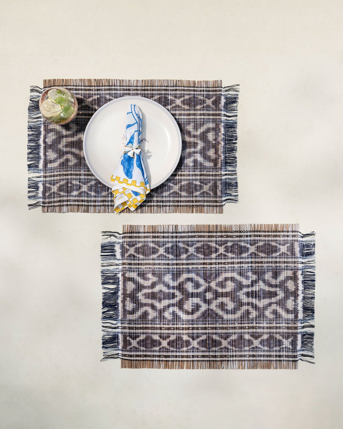 Pair of Sitara Ikat Placemats in charcoal ikat set on a light table.