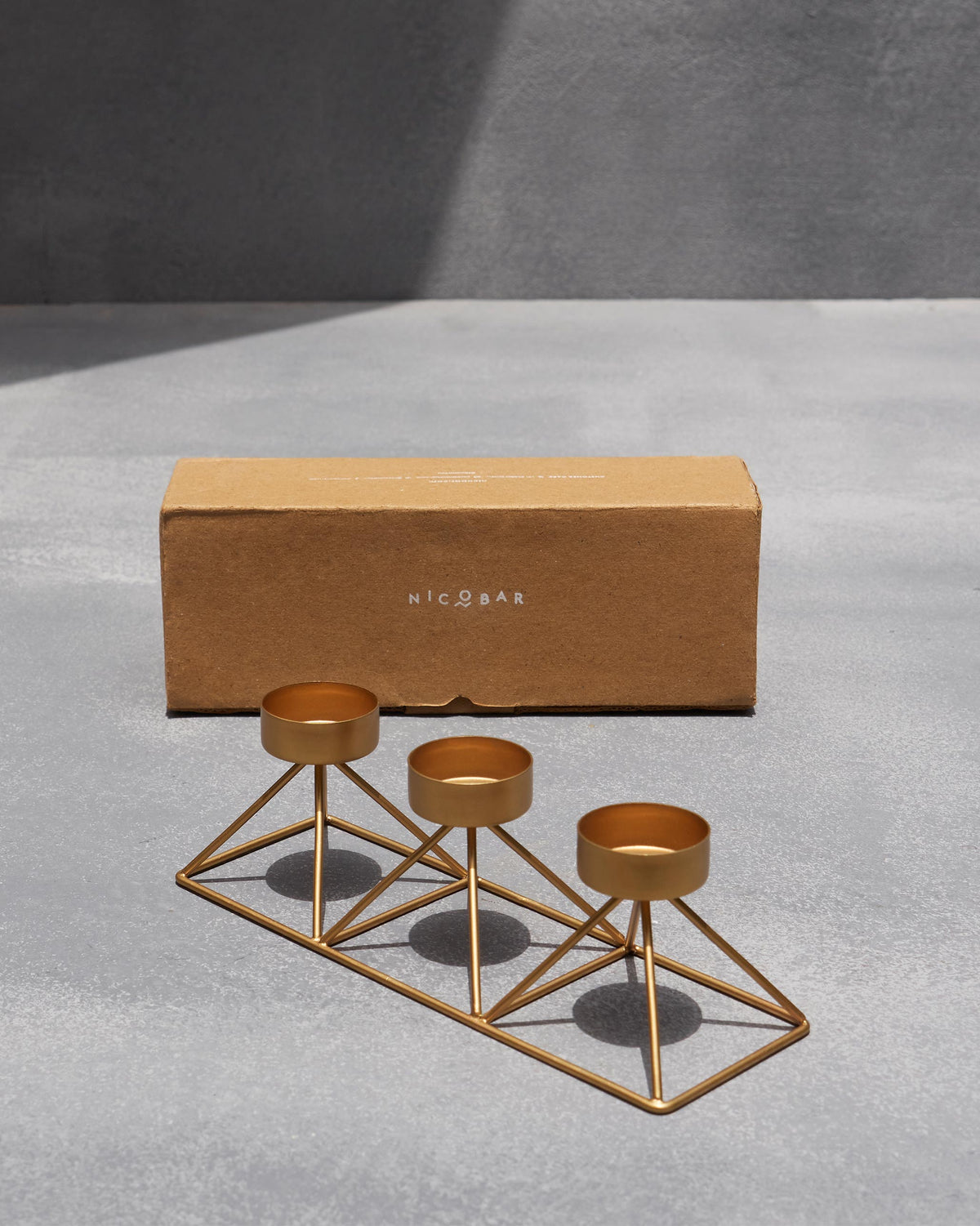 Myra Tealight Stand in front of its box on a grey surface.