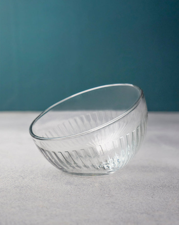 Clear fluted Mahi nut bowl tilted against a teal wall.