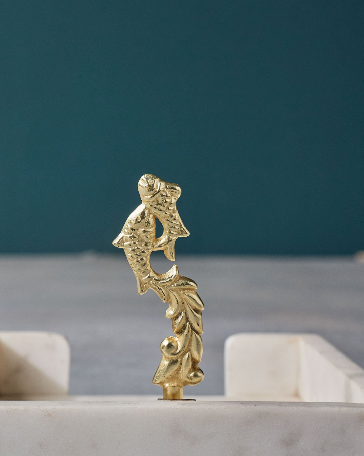 Gold fish-motif upright with leaf detail, standing on a Mahi Napkin Holder.