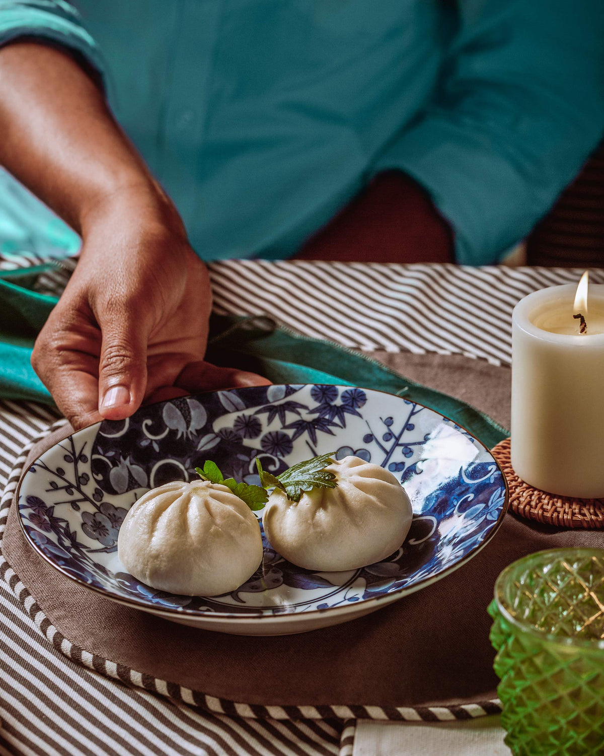 Blue floral Donburi shallow bowl held at the table with steamed buns inside.