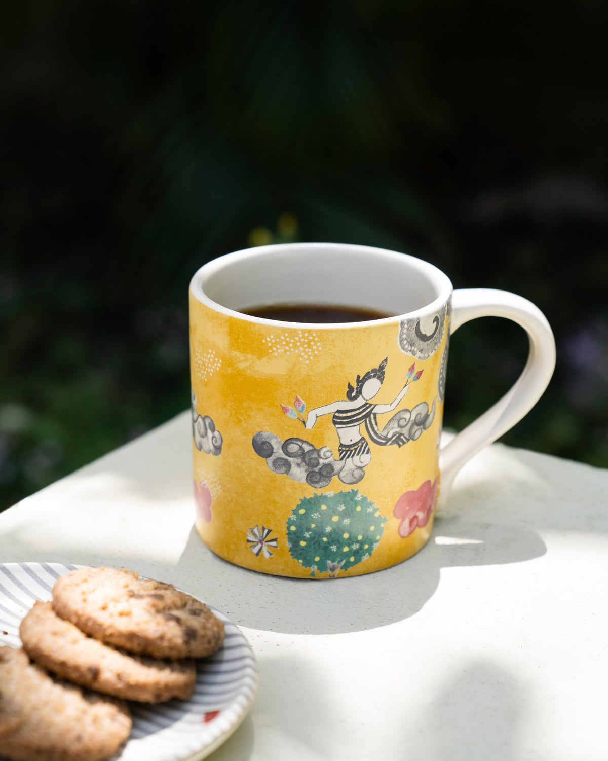 Bliss Mug filled with tea beside a plate of cookies.