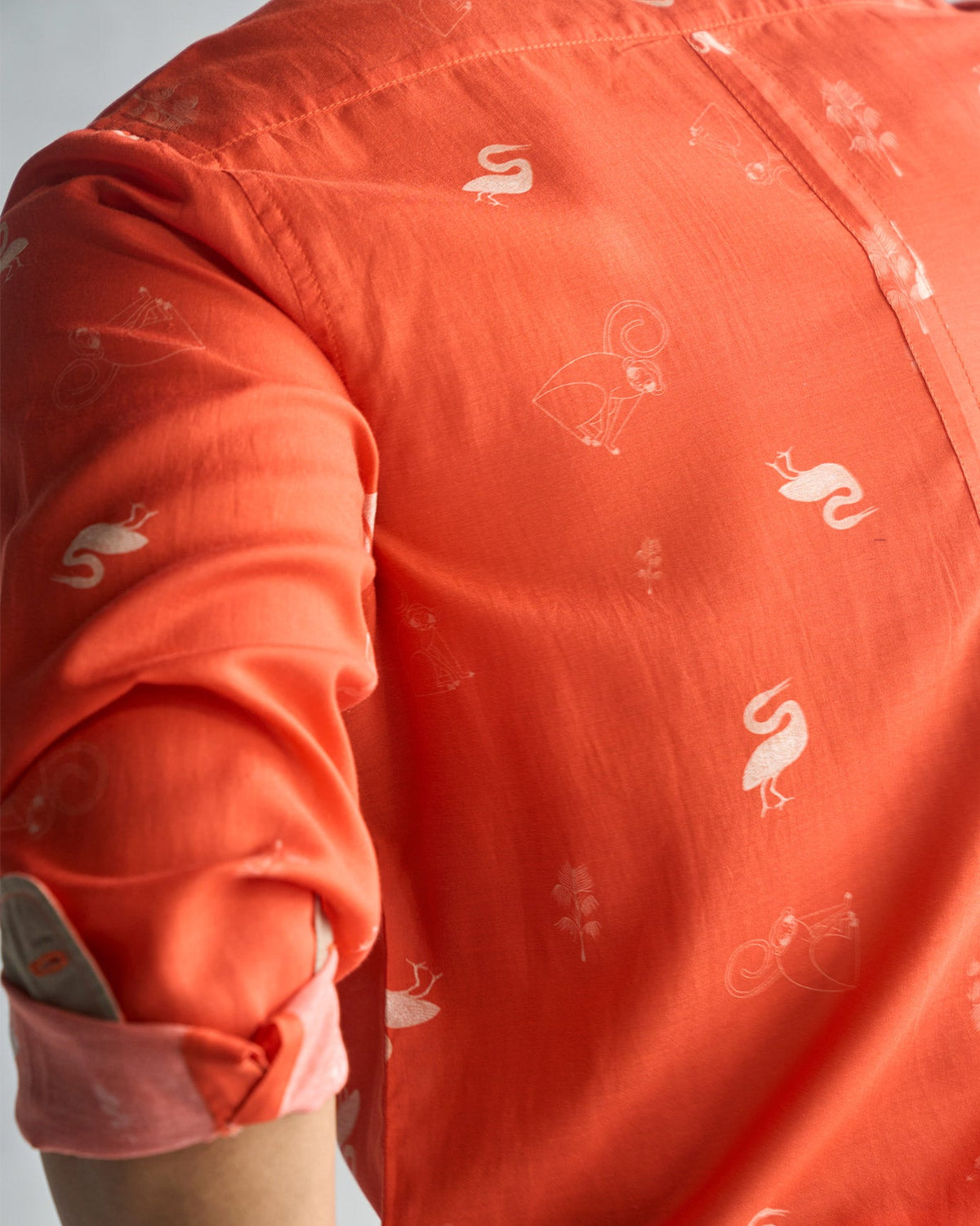 Close-up of a rust Paradise Shirt sleeve and body showing white bird motifs.