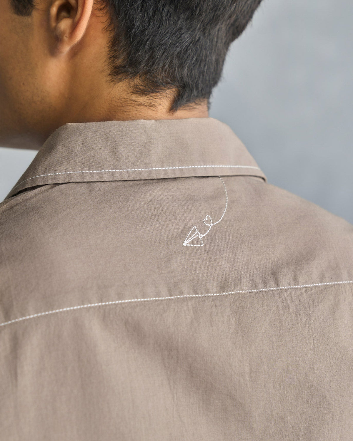Close-up of an oak brown Plateau shirt back showing a small white embroidered motif.