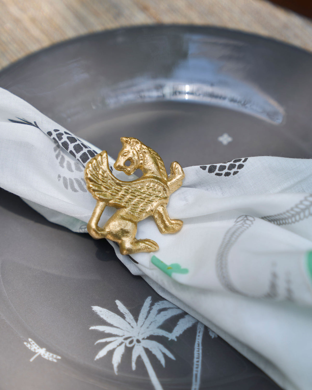 Brass Chinthe Napkin Ring holding a white printed napkin on a plate.