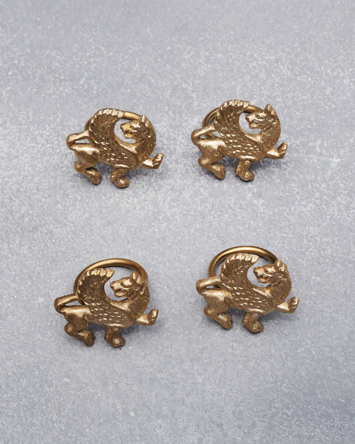 Overhead view of four brass Chinthe Napkin Rings arranged in a square.