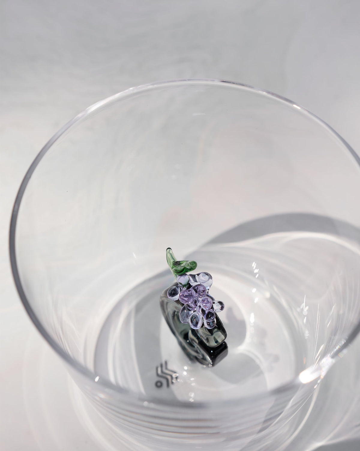 Looking down into a clear glass with purple flowers and a green leaf at the base.