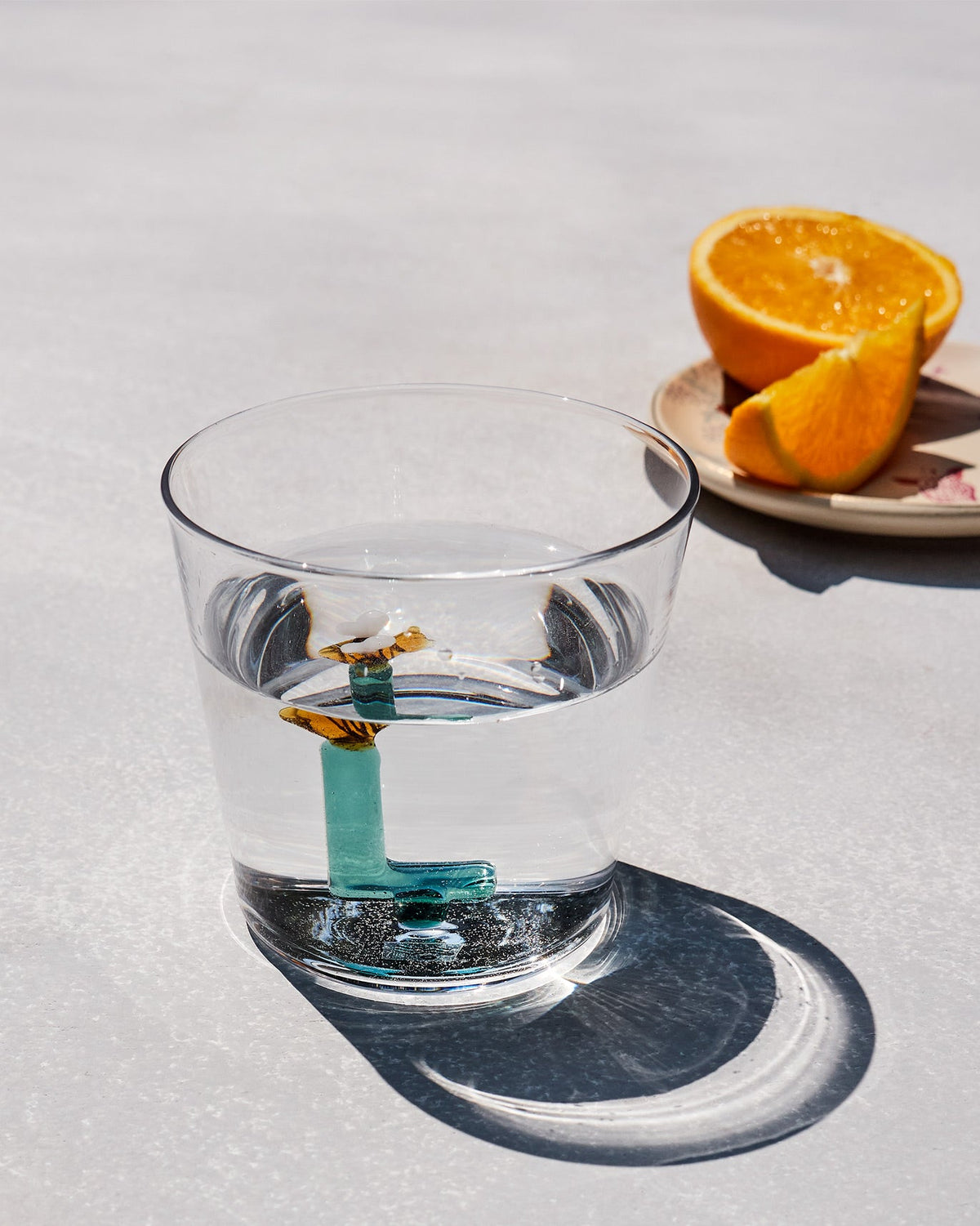 Clear Alphabet glass with a teal letter L and amber butterfly, half filled with water.