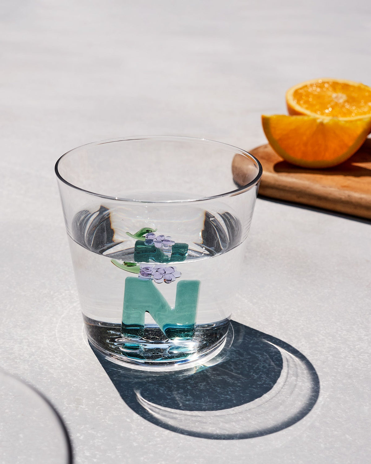 Clear Alphabet glass with a teal letter N and purple flowers, half filled with water.
