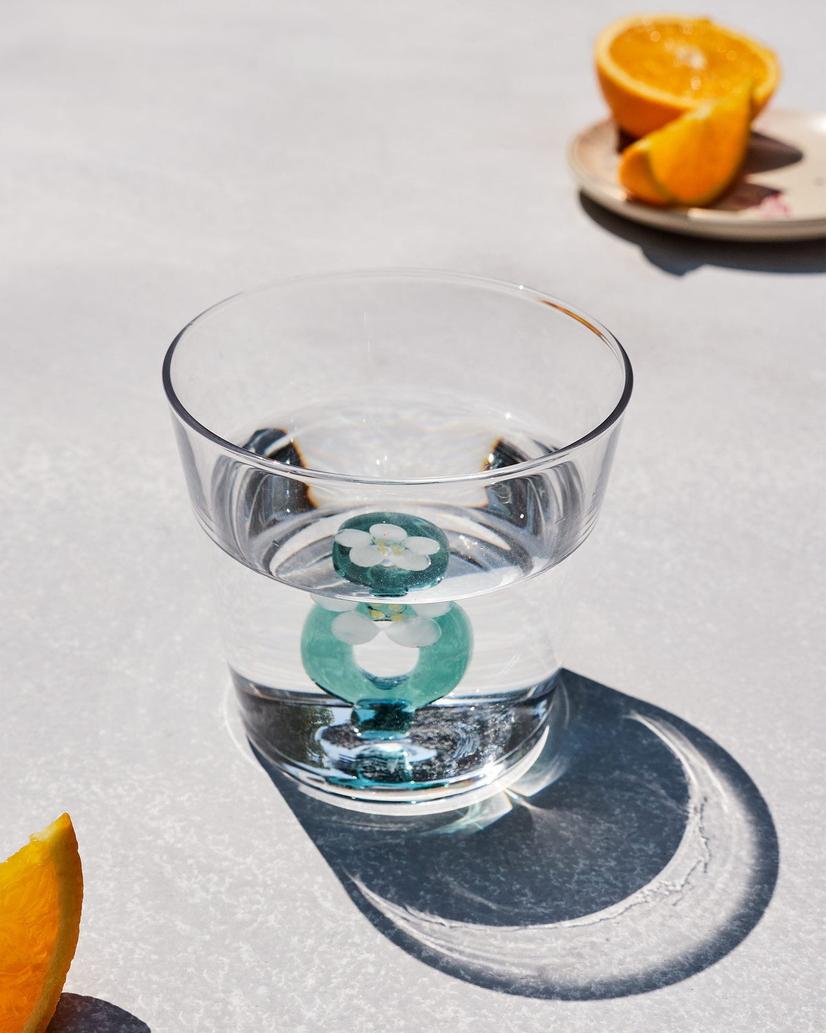 Clear Alphabet glass with a teal letter O and white flower, half filled with water.