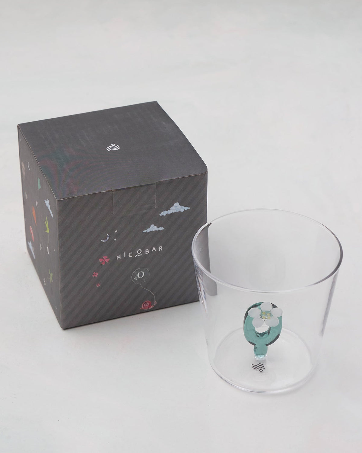 Alphabet glass with a teal letter O beside its charcoal Nicobar gift box.