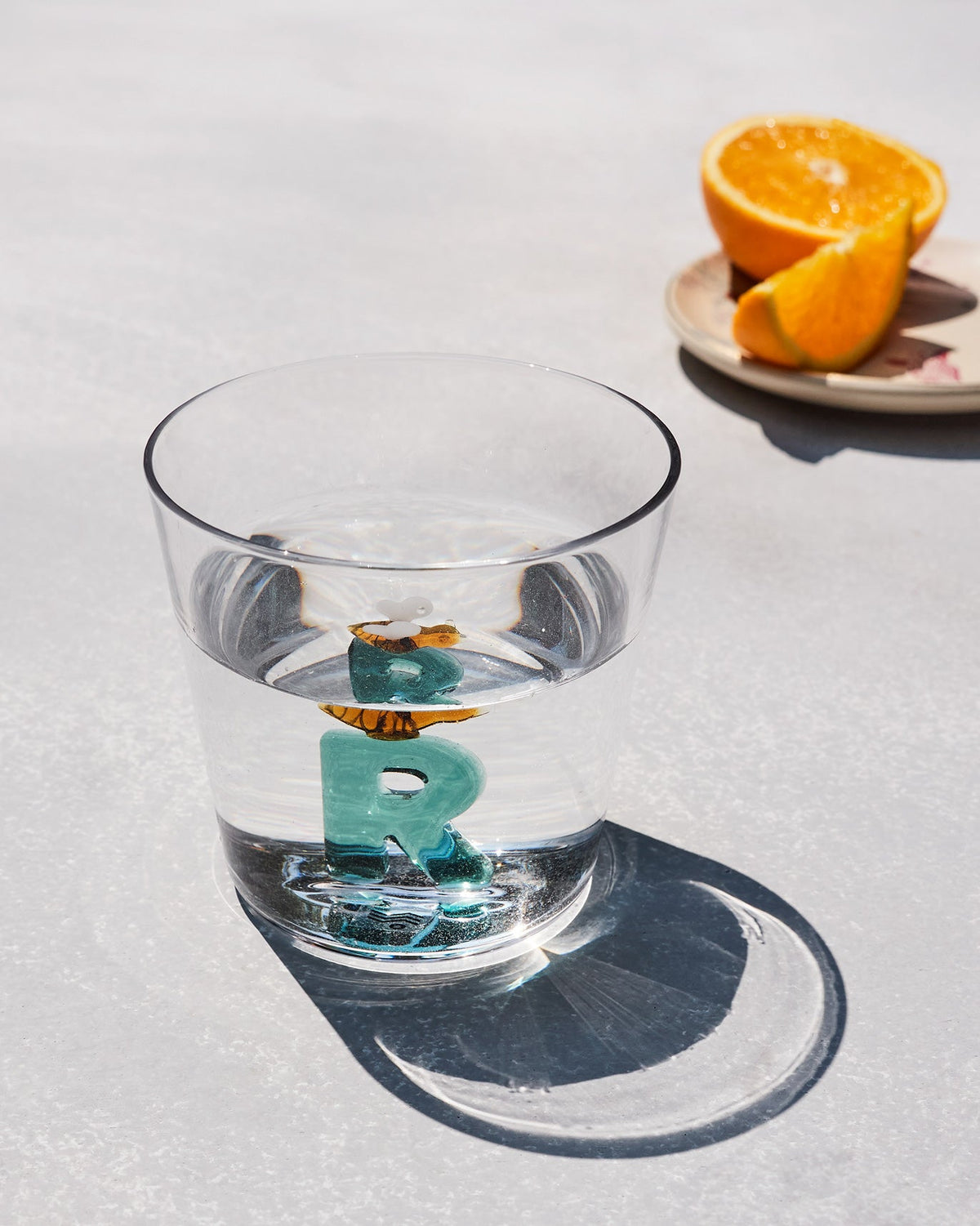 Clear drinking glass with a teal 3D letter R and a small bee at the base.