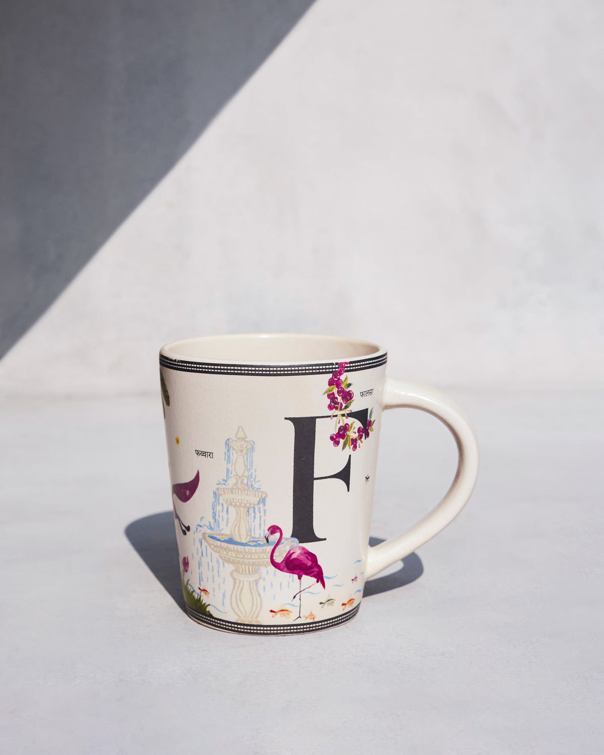 Cream Firefly mug with a black letter F, pink flamingo, and fountain motif.