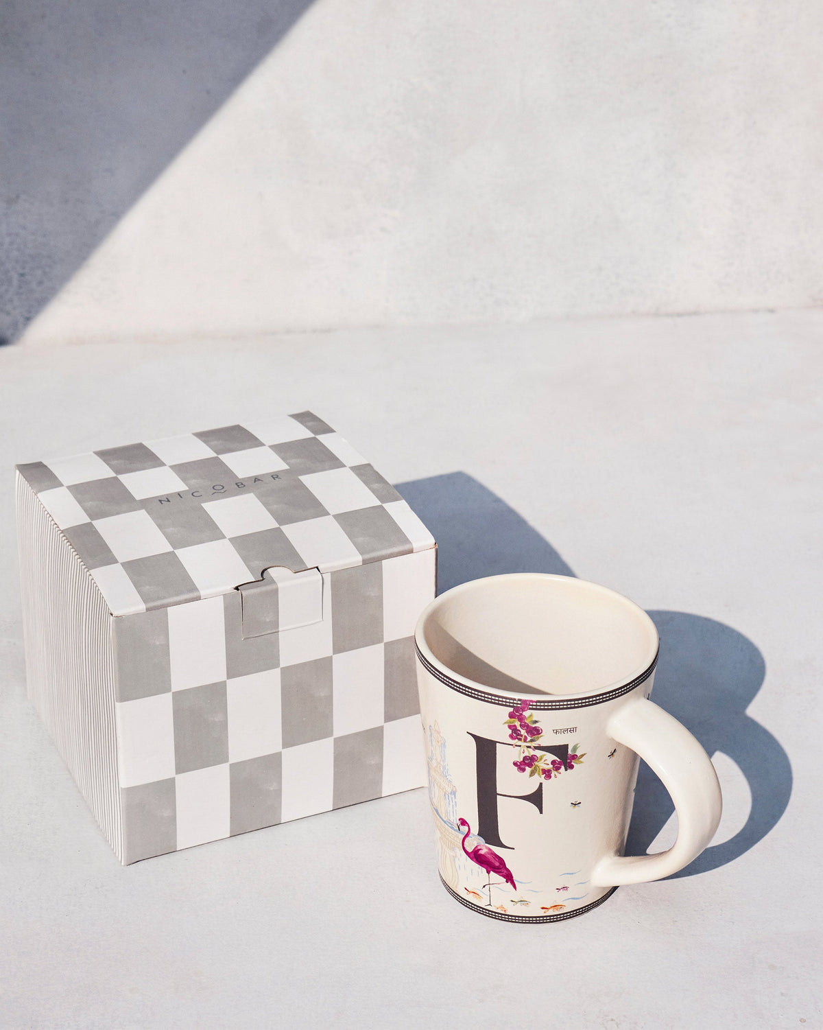 Firefly mug with letter F and flamingo beside a checkered Nicobar gift box.