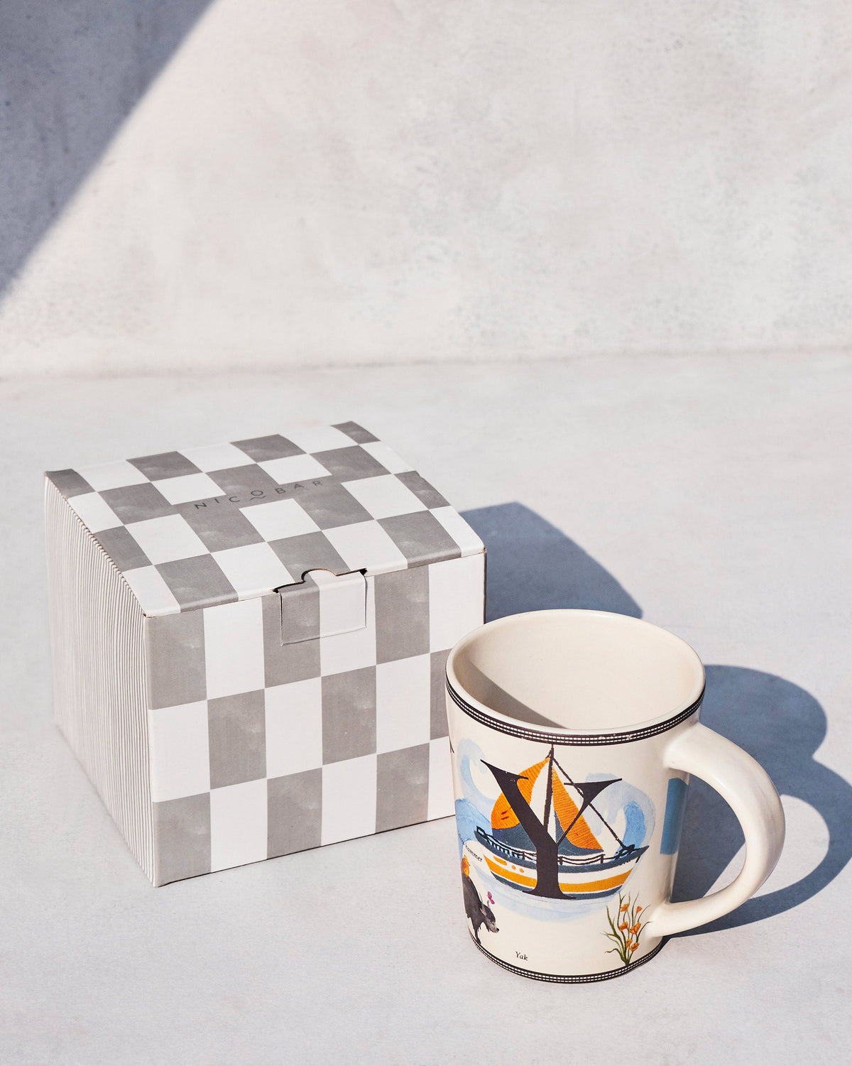 Cream Yoga alphabet mug beside a grey-and-white checked Nicobar gift box.