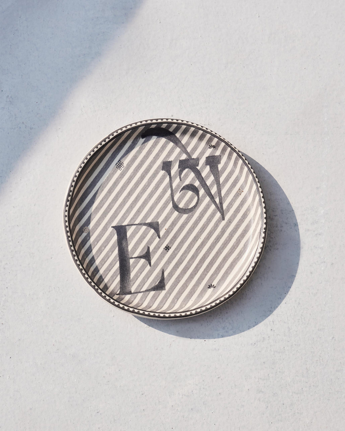 Akshar Coaster - E lying flat, showing the grey E glyph on diagonal stripes.