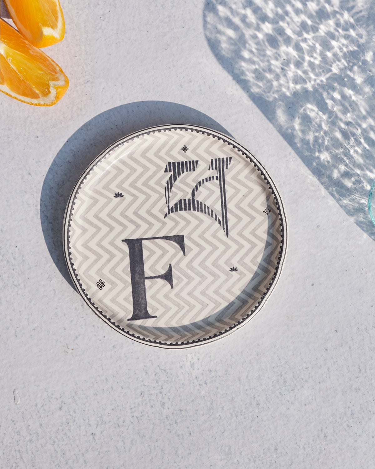 Akshar Coaster - F laid flat, showing the grey F glyph on a chevron pattern.