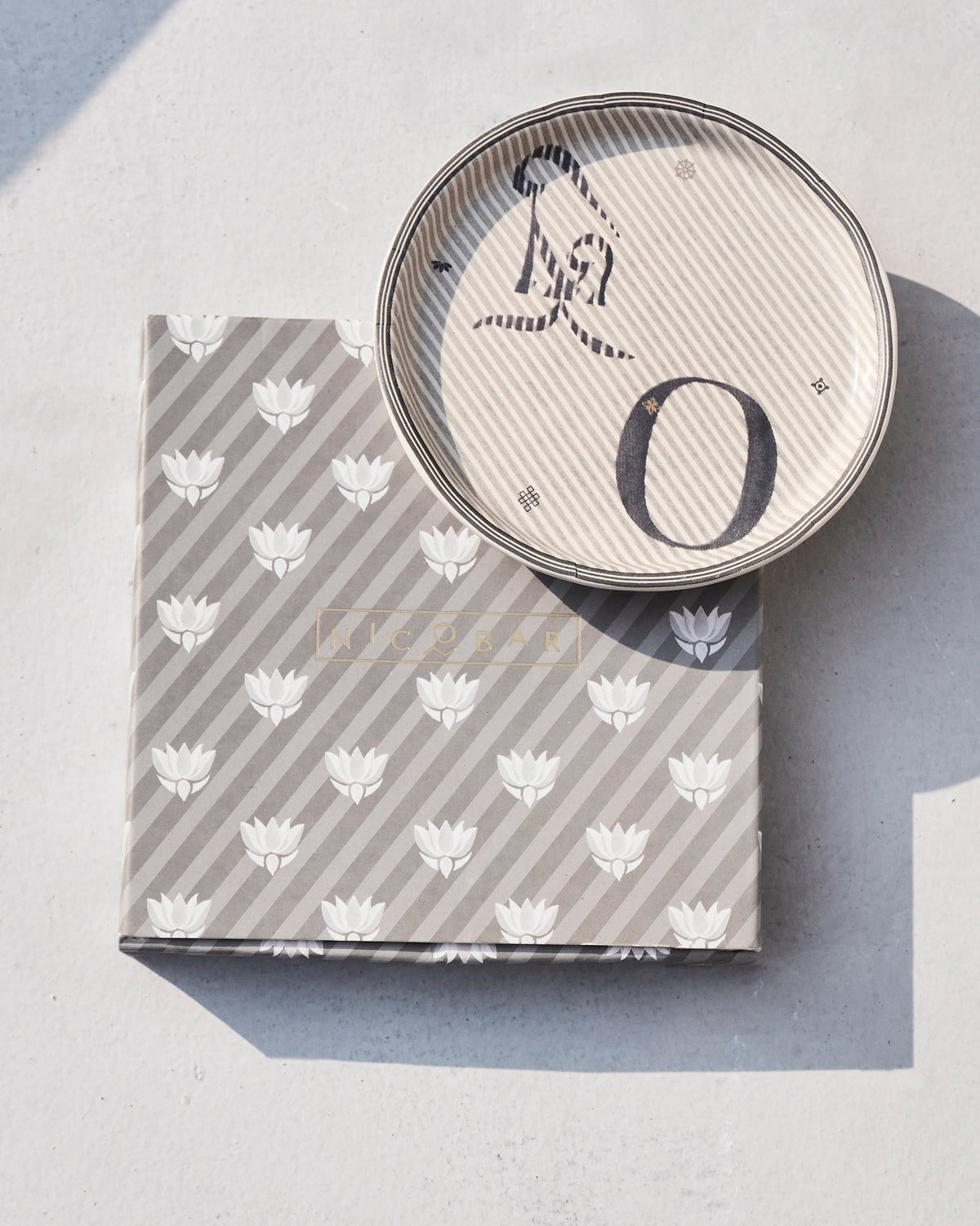 Akshar Coaster - O resting on its grey lotus-print box.