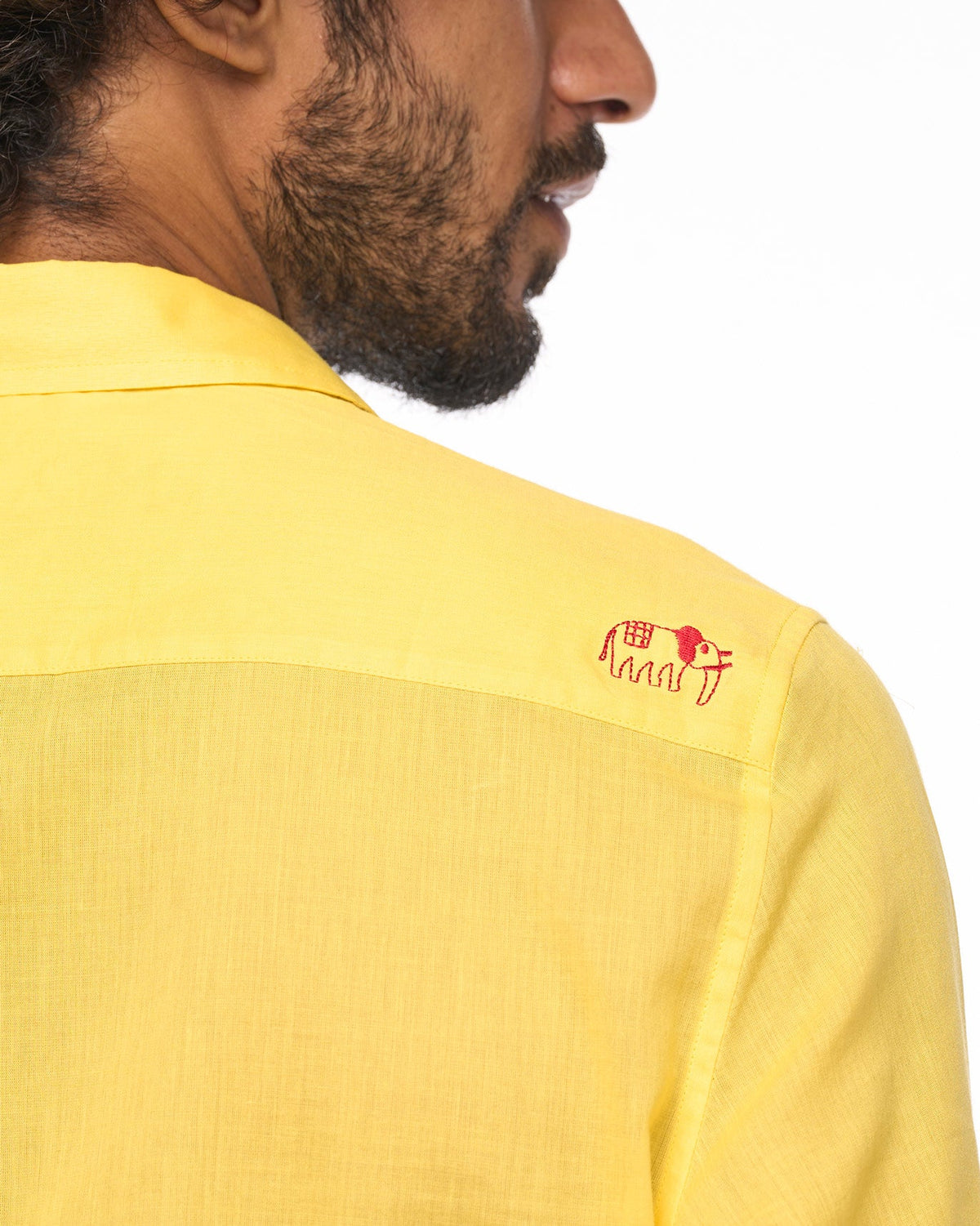 Close-up of a yellow Sankara shirt showing a small red embroidered motif on the shoulder.
