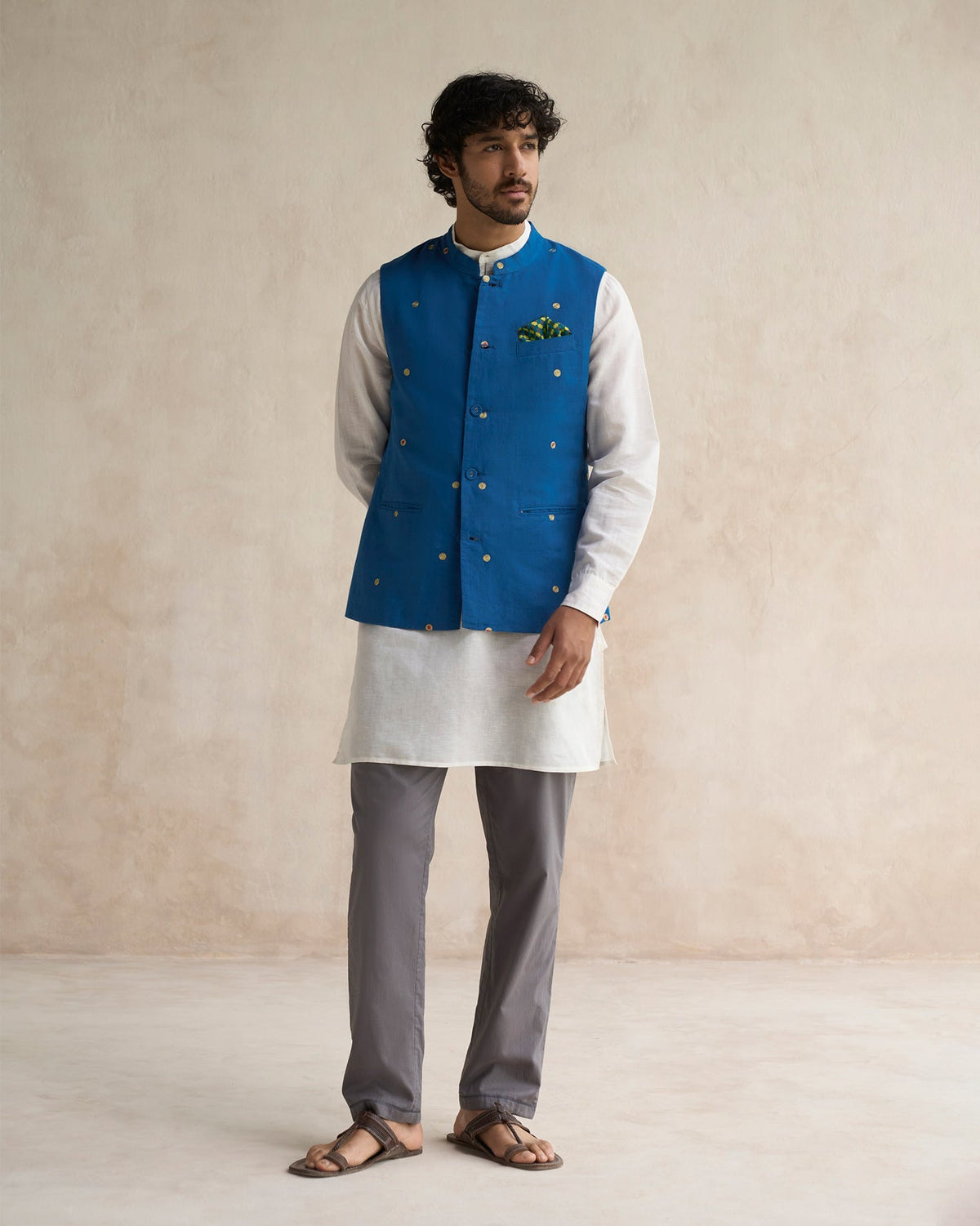 Person standing in a sapphire Nehru jacket with gold embroidered dots.