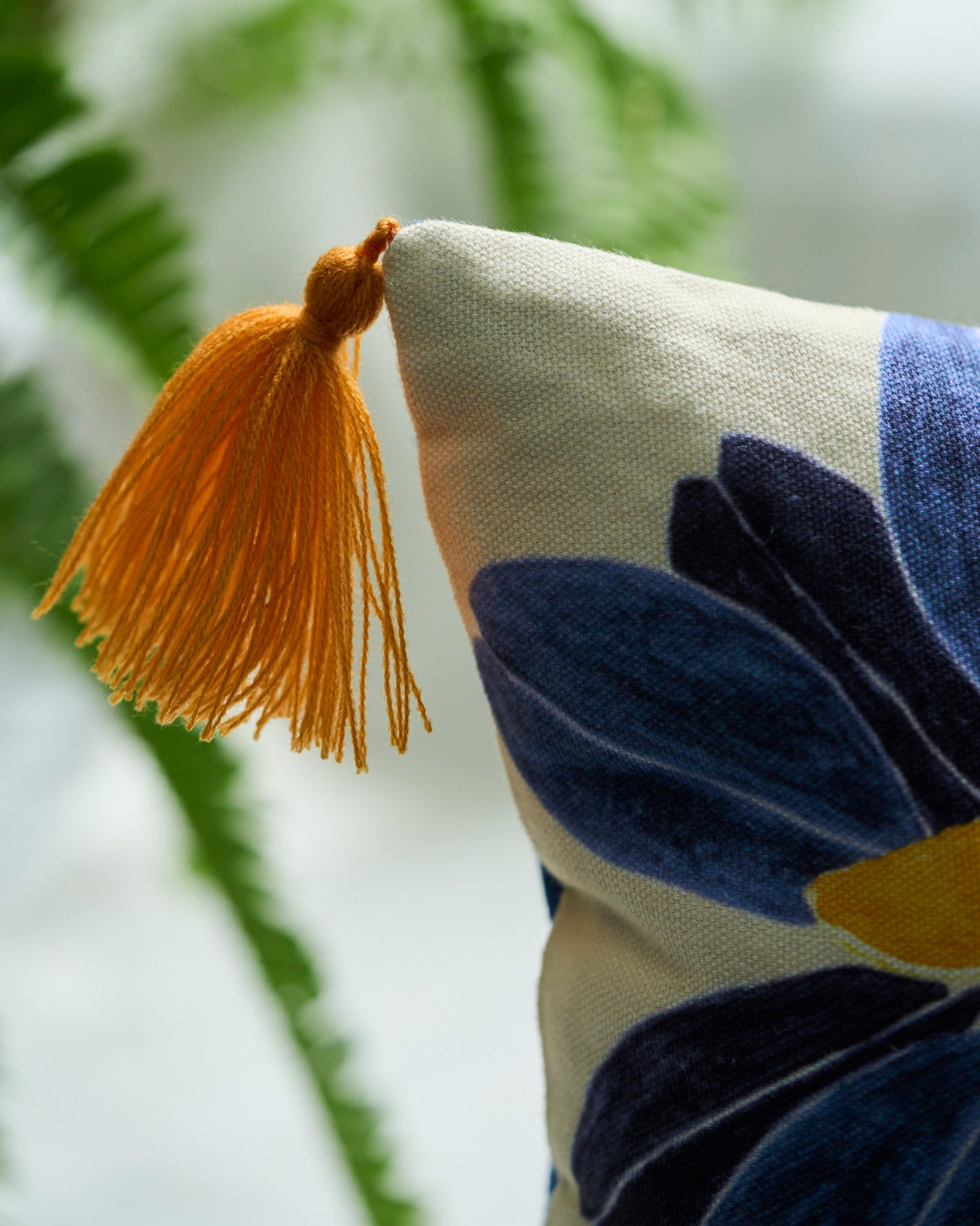 Close-up of the Bunga Lumbar Cover showing an orange tassel and indigo flower.