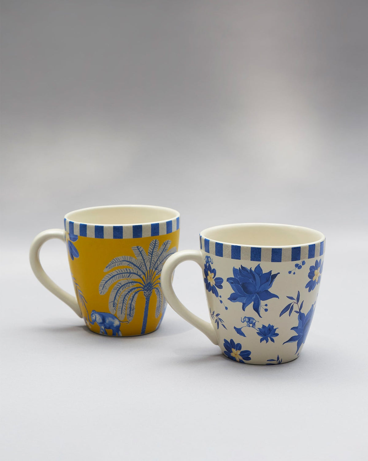 Yellow Panas mug with a palm and elephant beside a cream floral Panas mug.