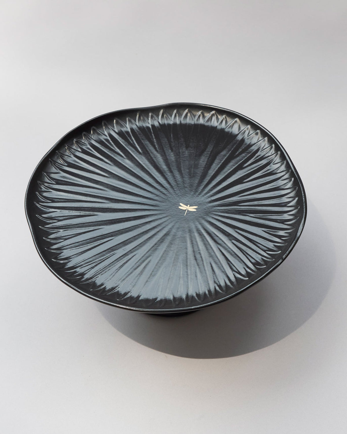 Top of the black Dragonfly cake stand showing radial ridges and a small gold dragonfly.