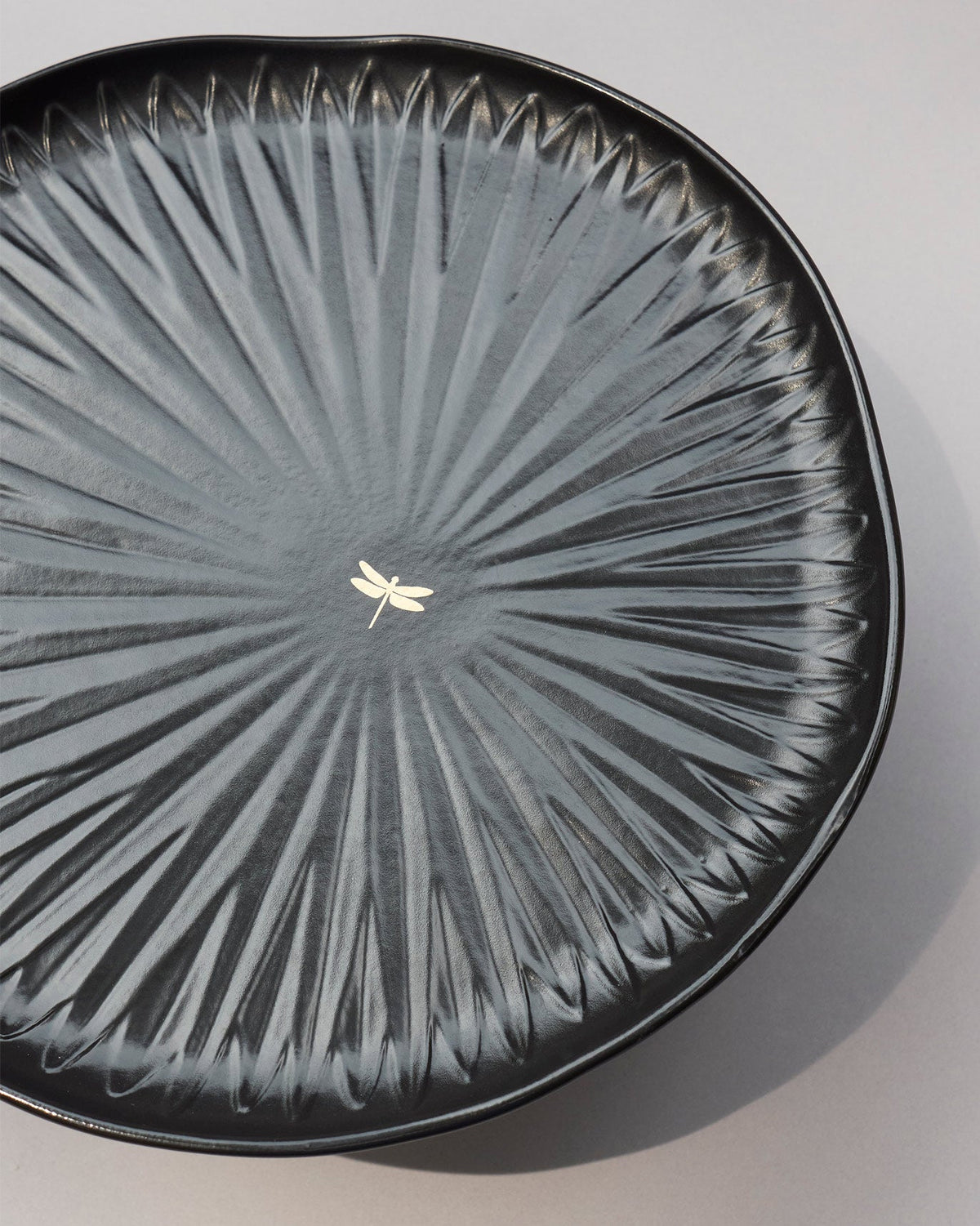 Close-up of the centre of a black cake stand showing a small gold dragonfly.