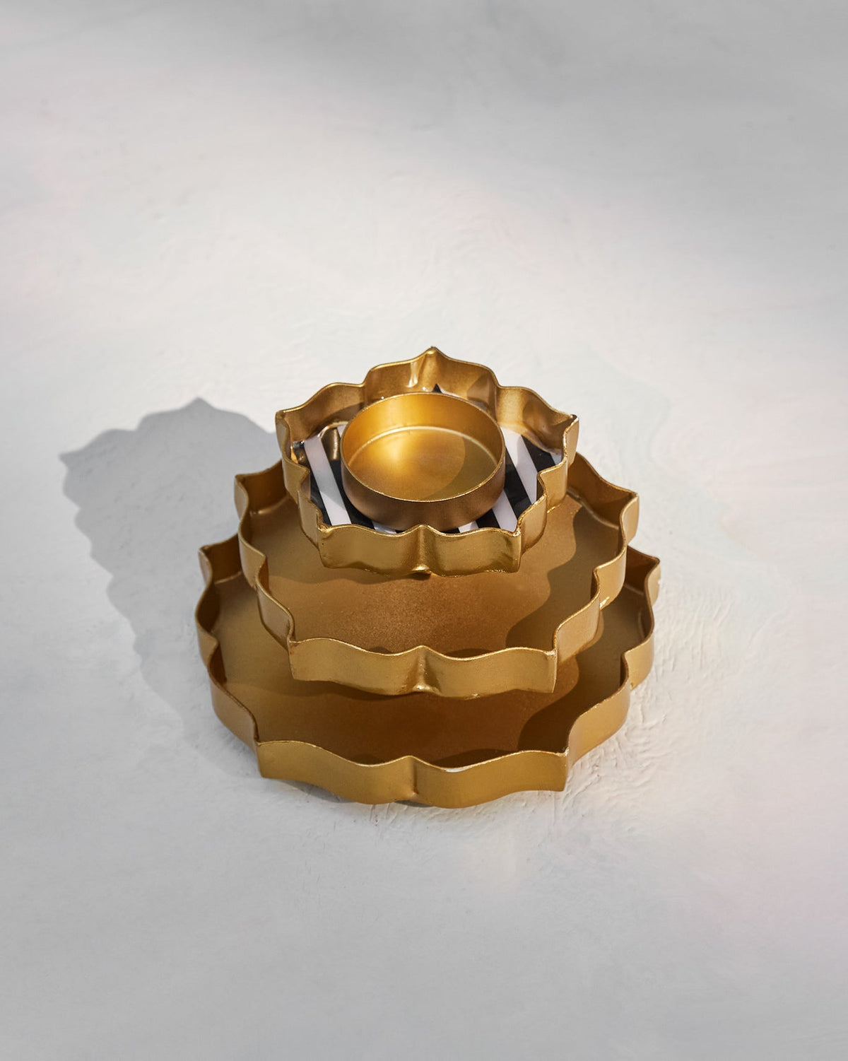 Nested gold Sama votive trays stacked from largest to smallest.