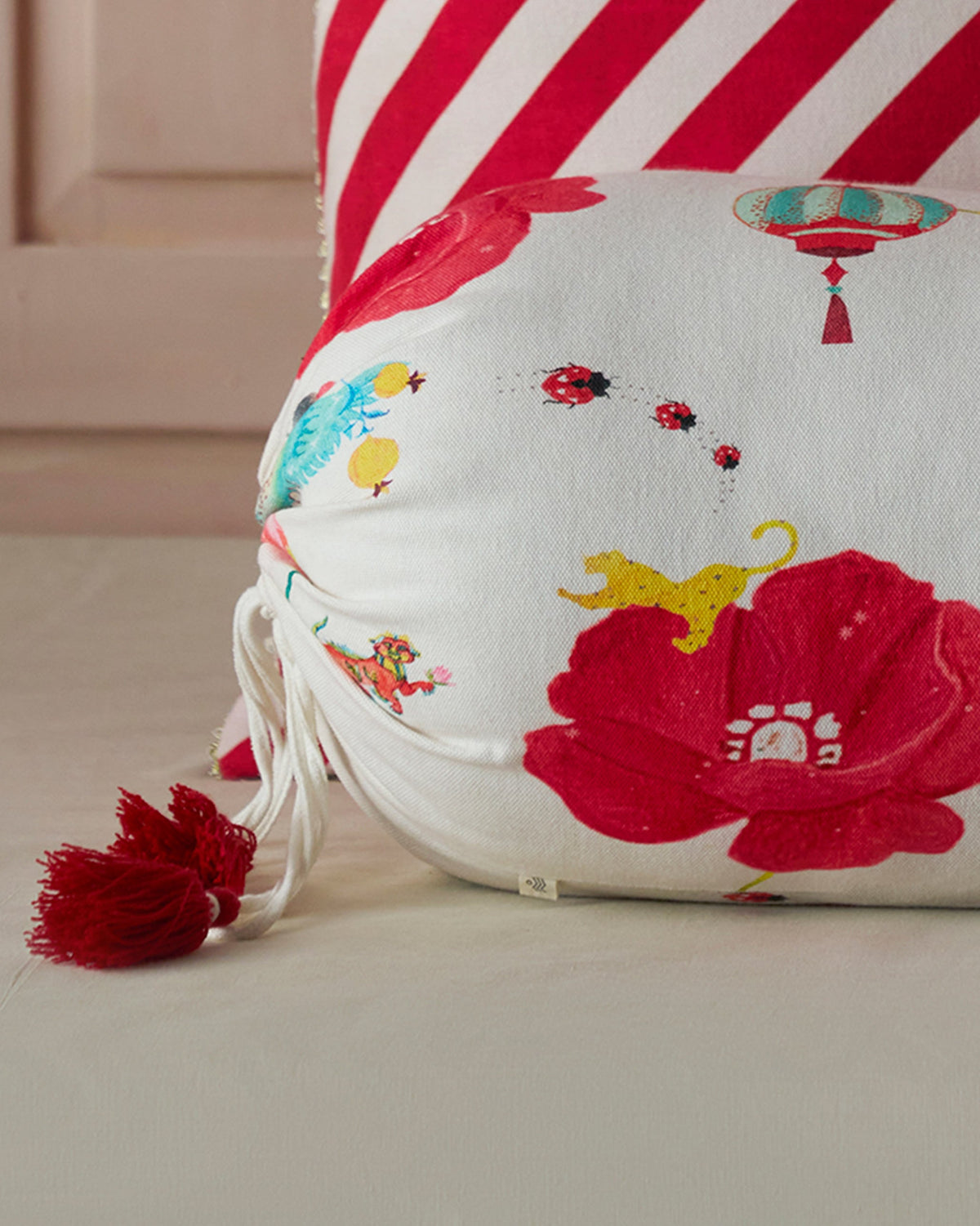 Close-up of Sphinx Bolster showing red poppies, a teal bird and tassel ends.